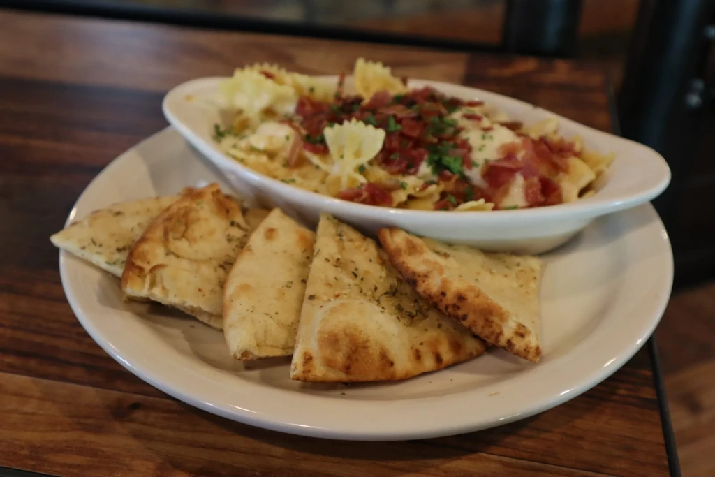 Top-down view: Creamy farfalle pasta with bacon, herbs, and flatbread.