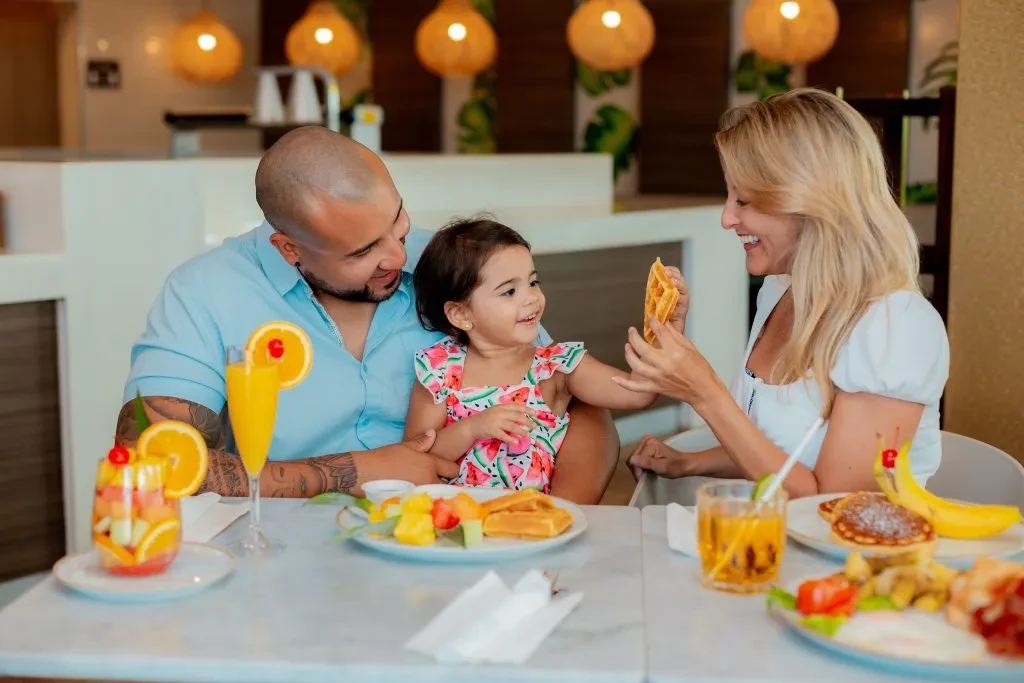 Happy family eats breakfast and fruit at a modern restaurant.
