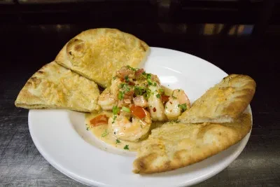 Plate of shrimp in creamy sauce with tomatoes, herbs, and flatbread.