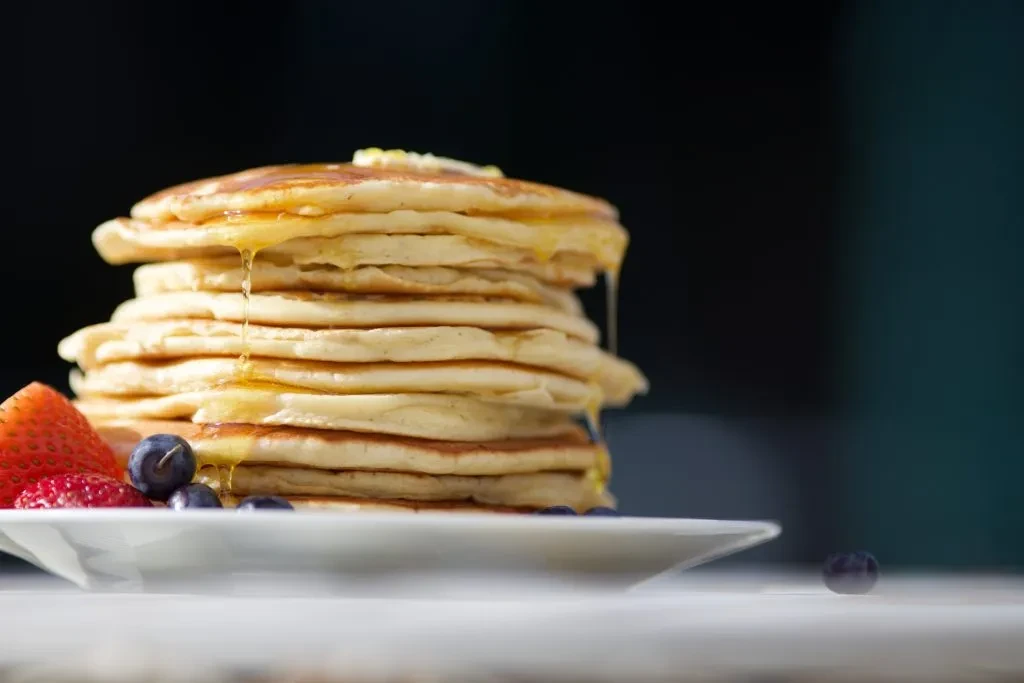Tall stack of syrupy pancakes with melting butter and fresh berries.