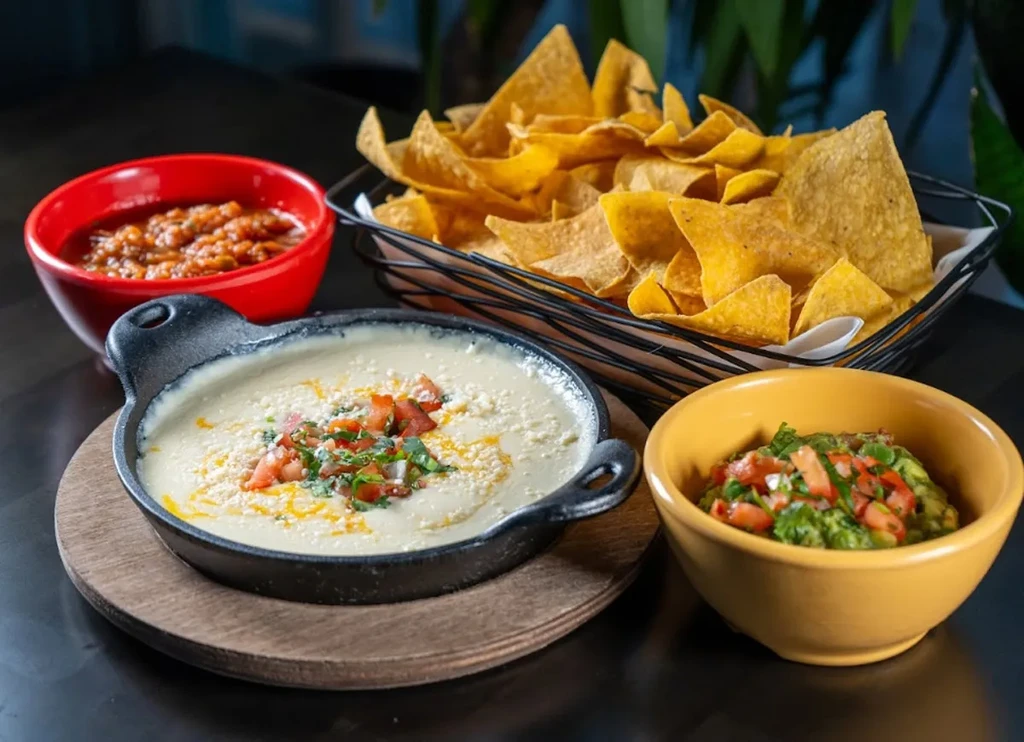 Mexican appetizers: queso dip, guacamole, salsa, and tortilla chips.