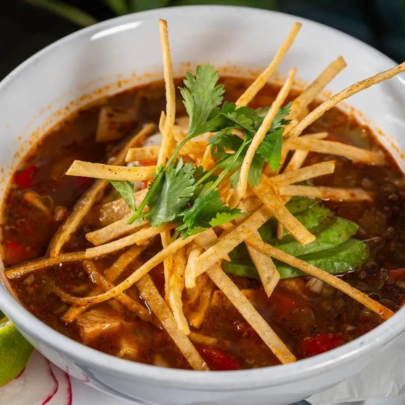 Top-down view of a garnished Mexican tortilla soup with chicken, avocado, and lime.
