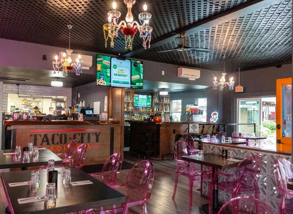 Eclectic restaurant interior featuring 'Taco City' bar, pink chairs, and chandeliers.