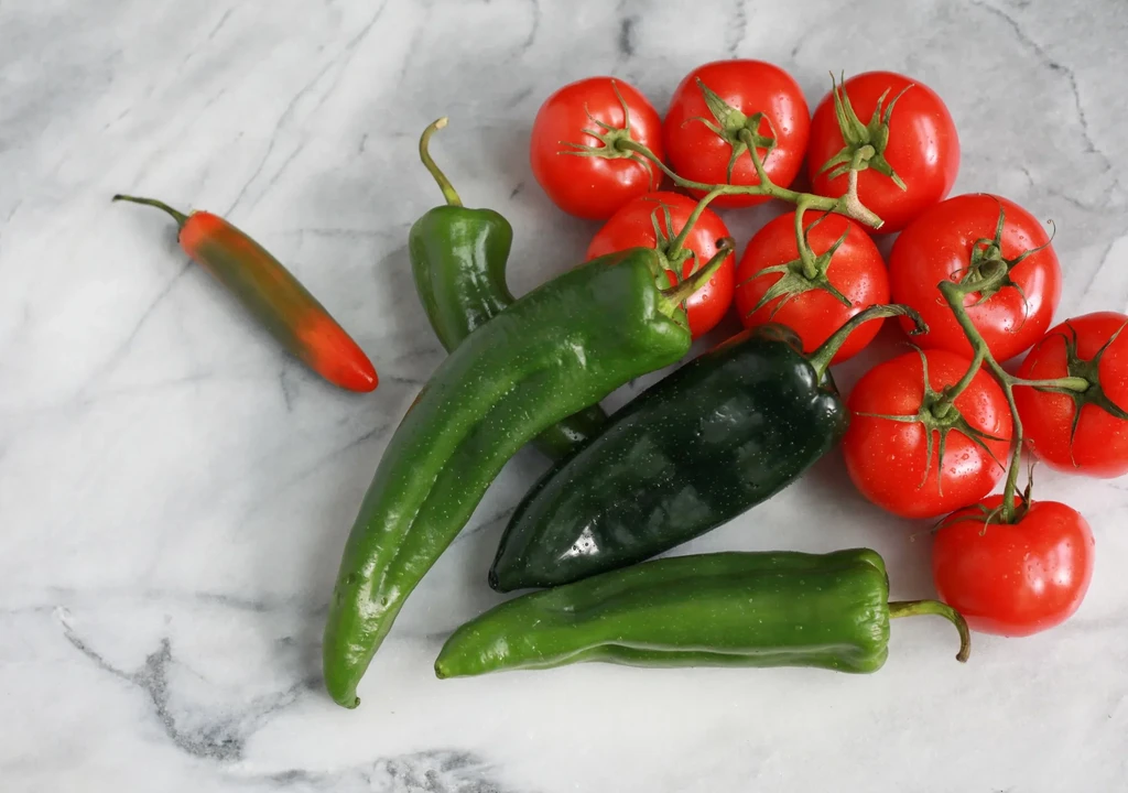 Fresh red tomatoes, green chilies, and one bicolored chili.