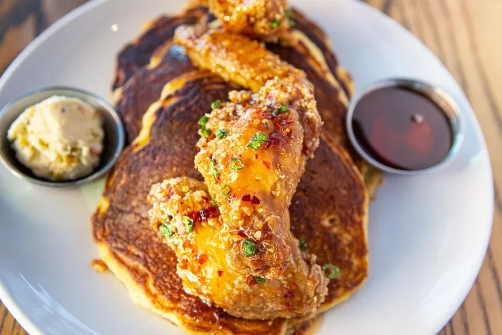 Pancakes with glazed fried chicken, green onions, red chili, butter, and syrup.