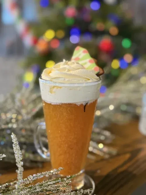 Festive drink with whipped cream, Christmas tree cookie, and bokeh lights.