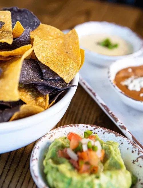 Colorful tortilla chips and three Mexican dips on a rustic table.