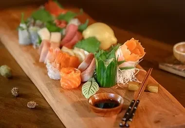 Platter of sushi, sashimi, rolls, and garnishes on a wooden board.
