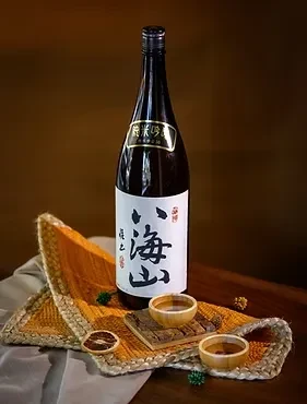 Dark glass sake bottle, wooden bowls, citrus slices, green sprigs.