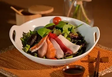 Sashimi salad with fish, shrimp, roe, greens, and chopsticks.
