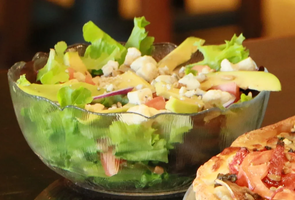 Fresh salad in a glass bowl and a partial pizza slice.