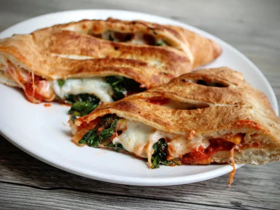 Two golden-brown calzones filled with cheese, spinach, and tomato sauce.