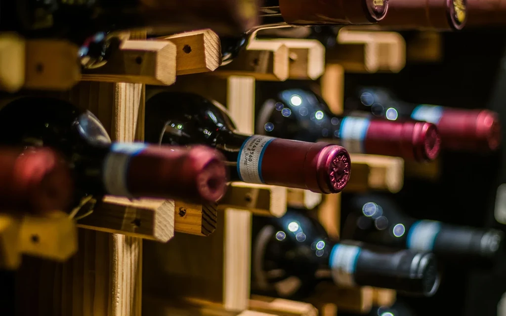 Dark wine bottles with red caps neatly stored in a wooden rack.