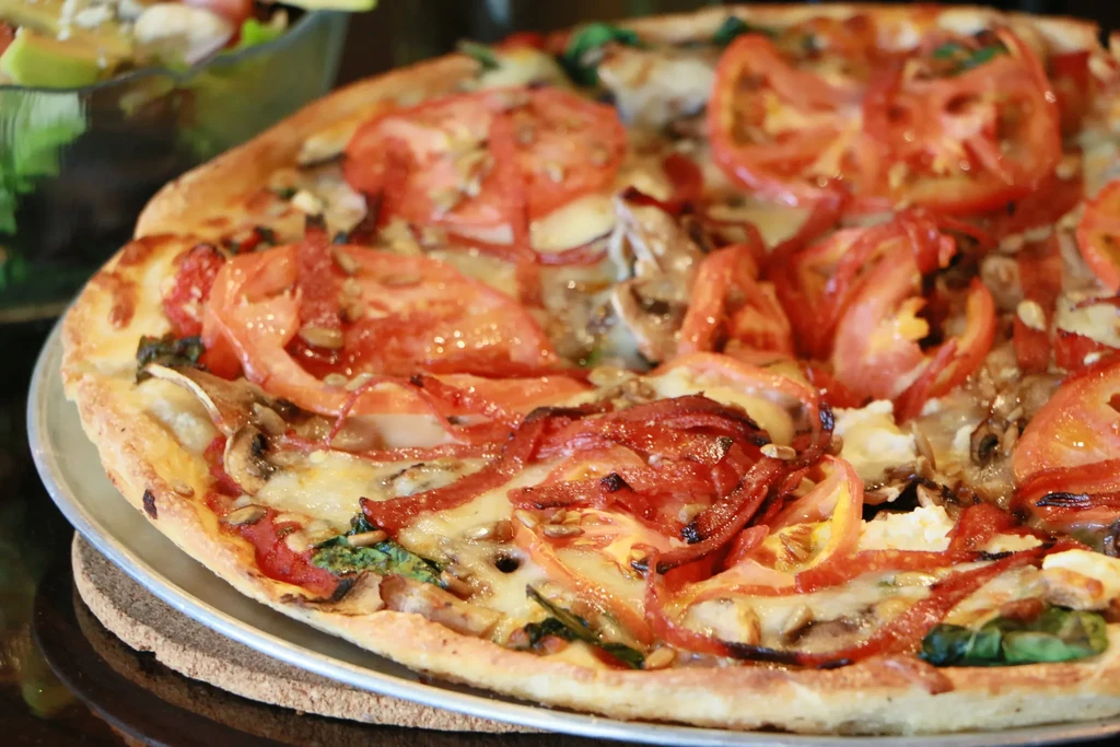 Freshly baked pizza topped with tomatoes, cheese, spinach, mushrooms, and nuts.
