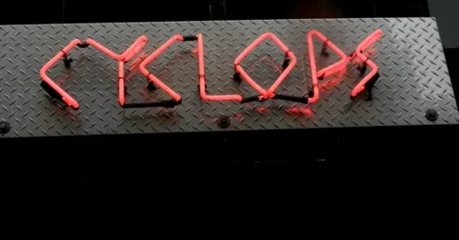 Bright red CYCLOPS neon sign mounted on metallic diamond plate.