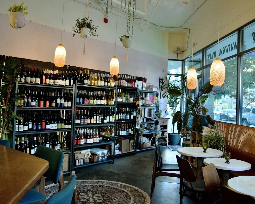 Interior of a bright natural wine bar with shelves of bottles and seating.