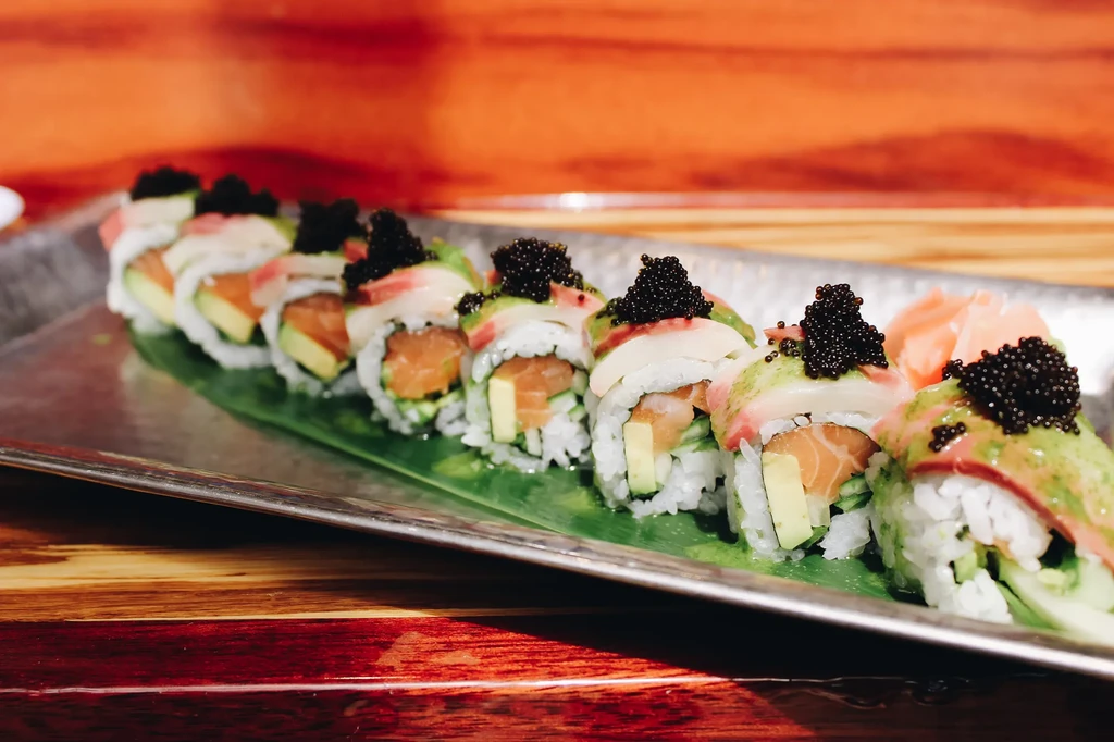 Platter of elaborate sushi rolls topped with fish, avocado, and black caviar.