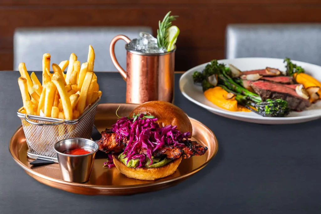 Restaurant meal spread: burger, fries, steak, roasted vegetables, Moscow Mule.