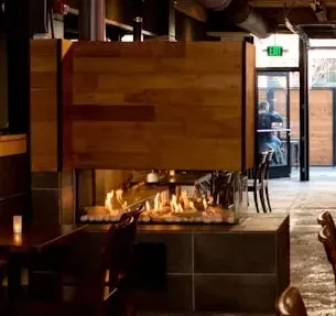 Modern double-sided fireplace with orange flames in an industrial restaurant.