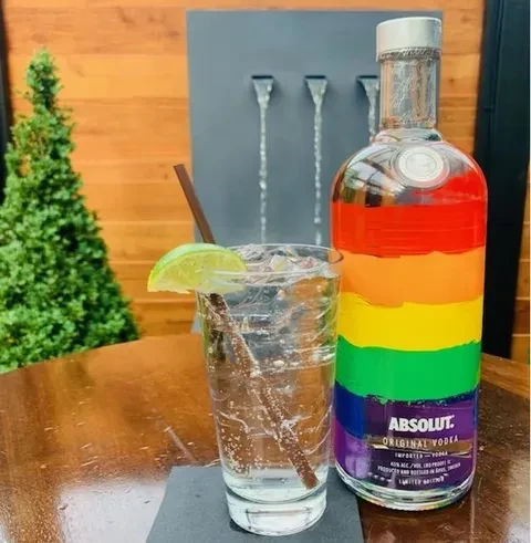 Absolut Pride vodka bottle and a clear drink with lime and straw.