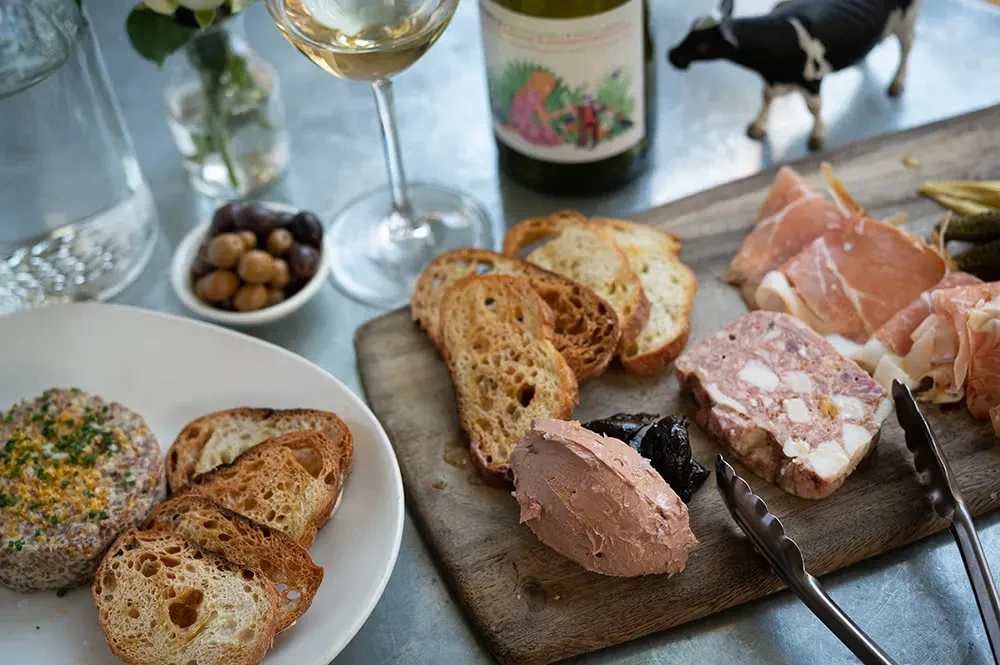 Table spread with charcuterie, pâté, tartare, wine, and olives.