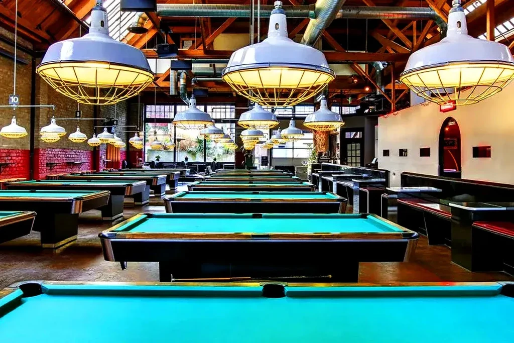 Industrial hall with turquoise pool tables, industrial lights, and booth seating.