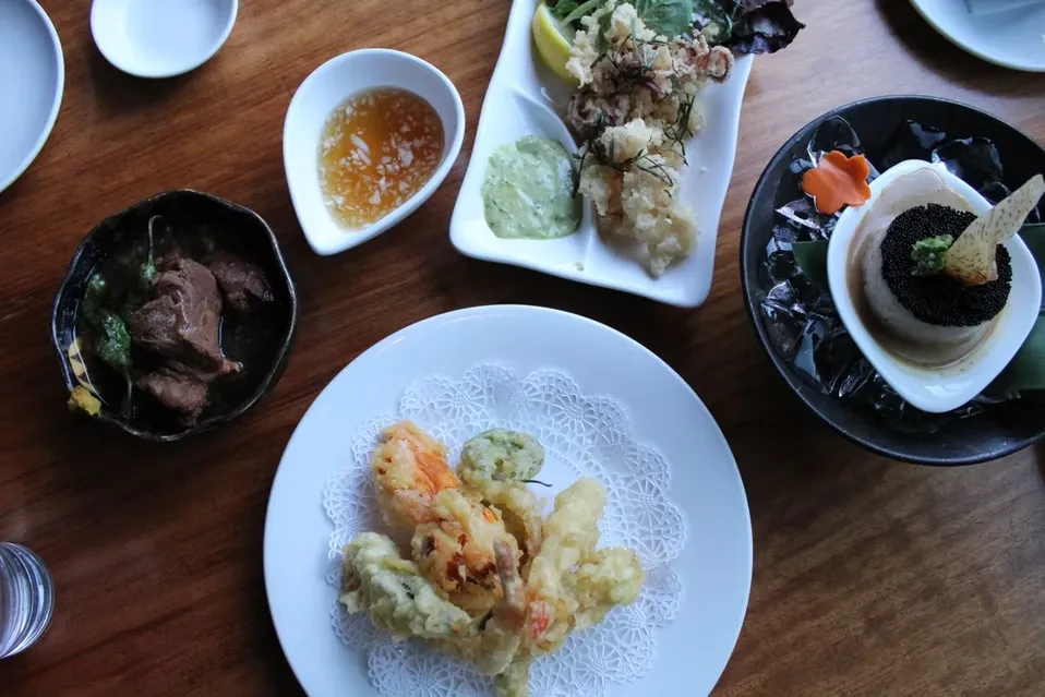 Overhead view of a multi-course meal with tempura, braised meat, and caviar.