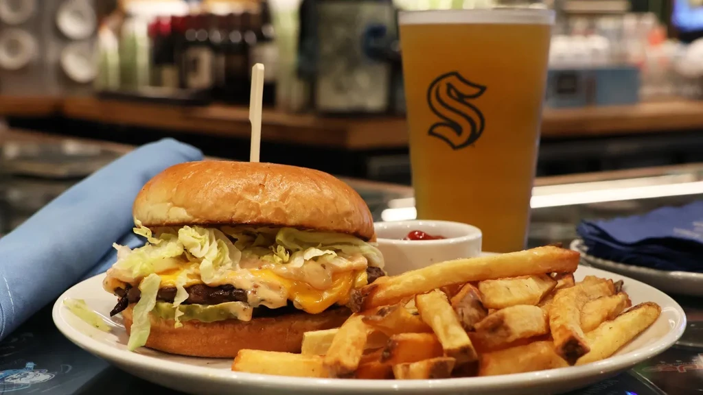 Burger, french fries, ketchup, and amber beer on a white plate.