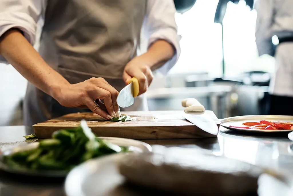 Chef's hands chopping green herbs with a knife on a cutting board.