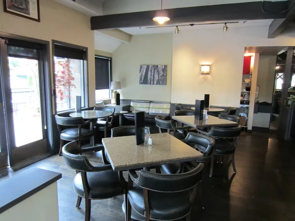 Empty modern casual restaurant interior with dark chairs and light tables.