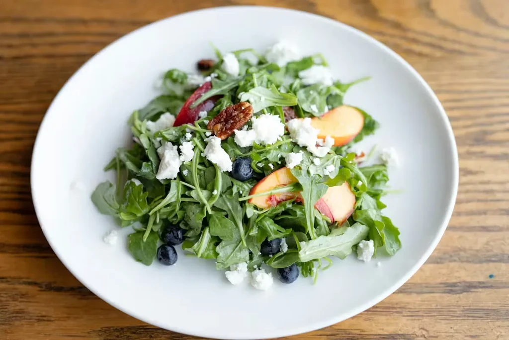 Fresh green salad with peaches, blueberries, crumbled cheese, candied nuts.