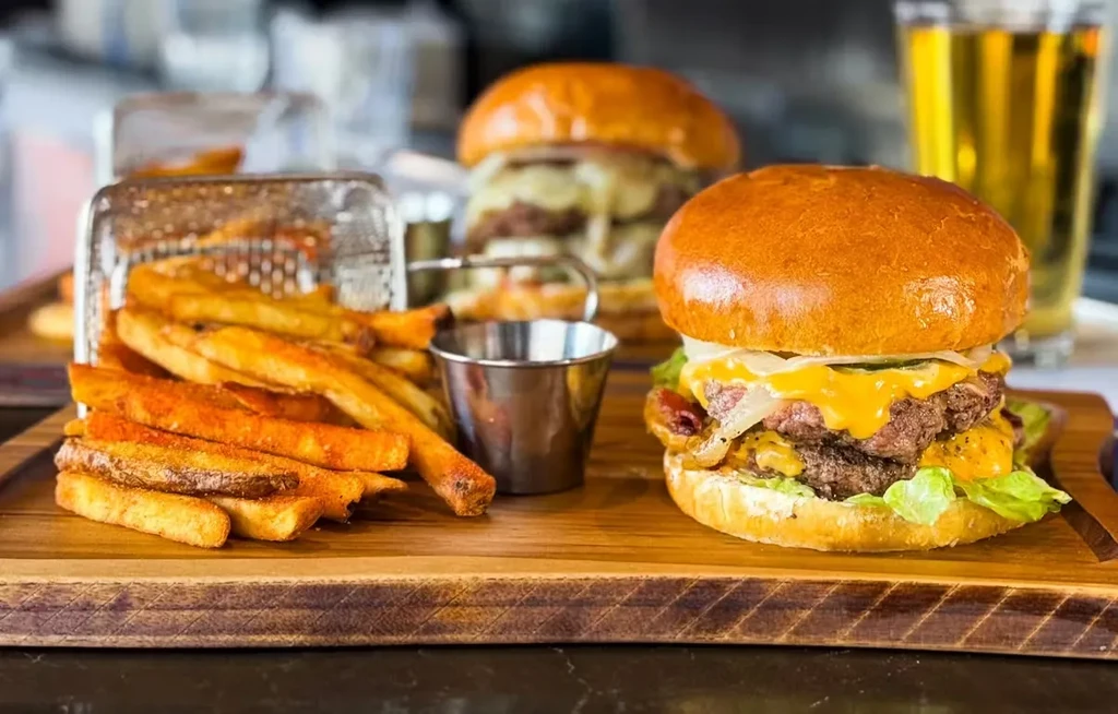 Two cheeseburgers, fries, and beer on a rustic wooden board.