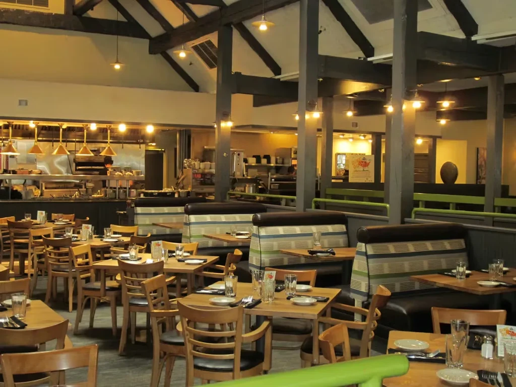Warmly lit restaurant interior with wooden tables, striped booths, and open kitchen.