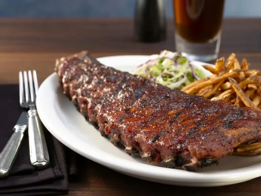 Full rack of glistening barbecued ribs with fries and coleslaw.