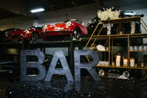 Large, dark 'BAR' letters, gold bar, and luxury cars on display.