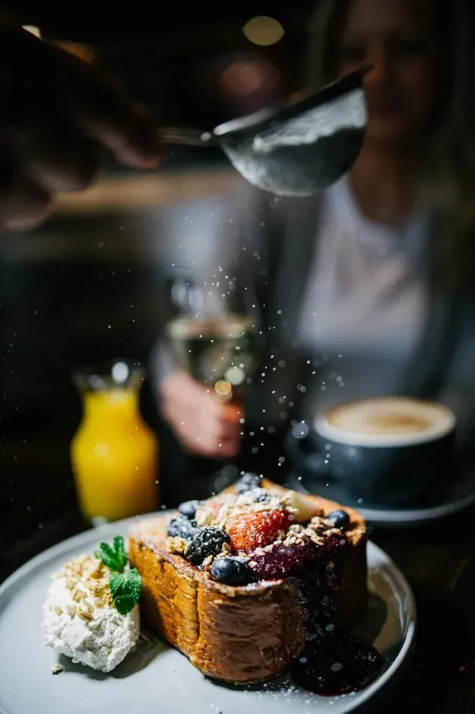 French toast with berries, granola, cream, and sifting powdered sugar.