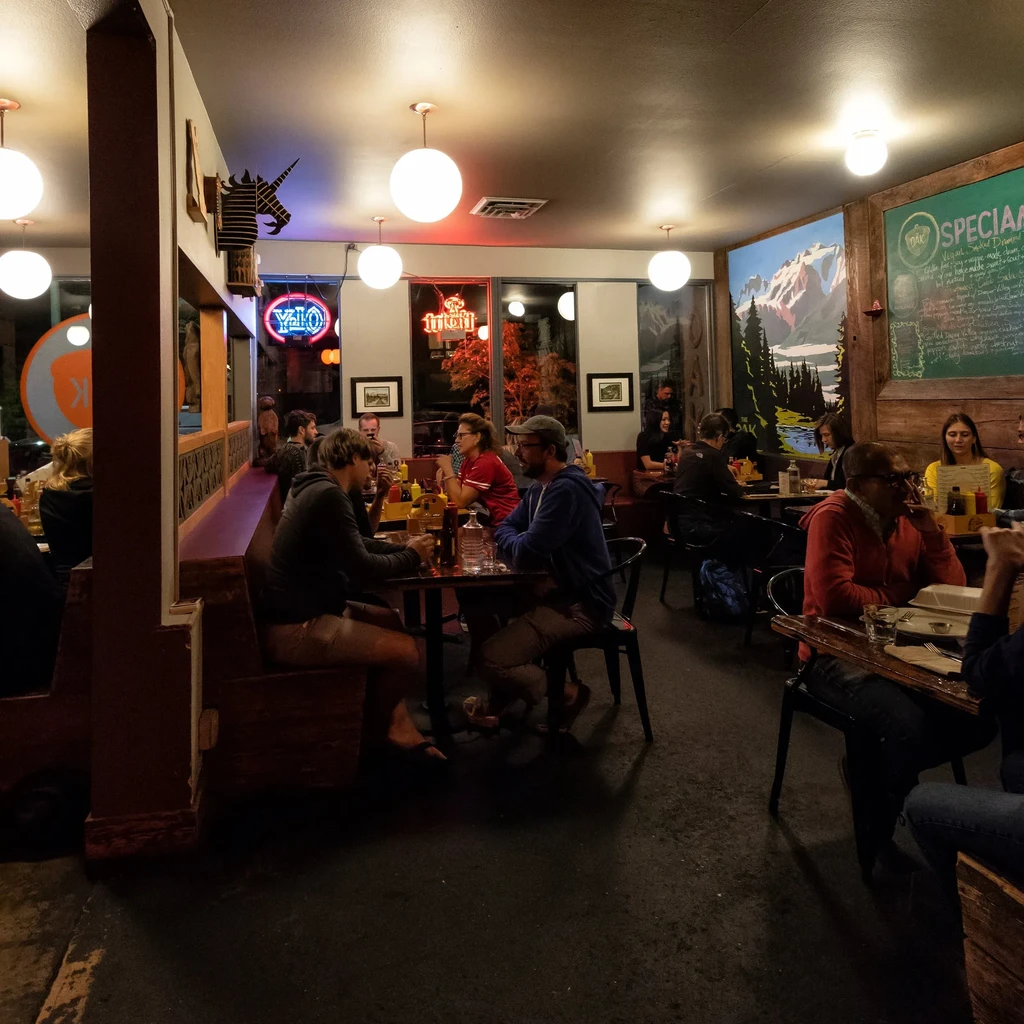 Bustling restaurant interior with patrons, mountain mural, and warm pendant lights.