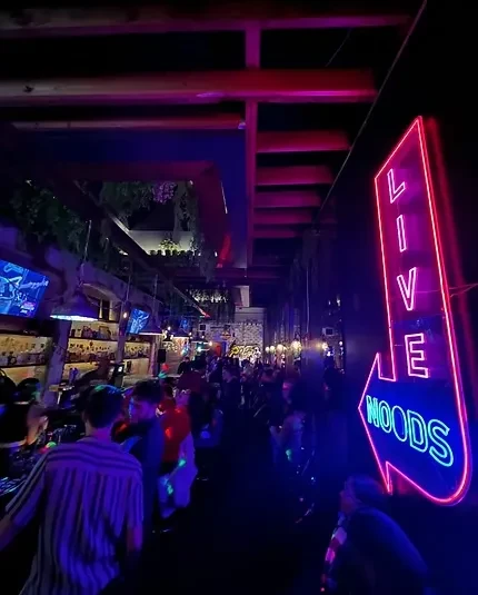 Lively bar with 'LIVE WOODS' neon sign, purple lights, and a crowd.