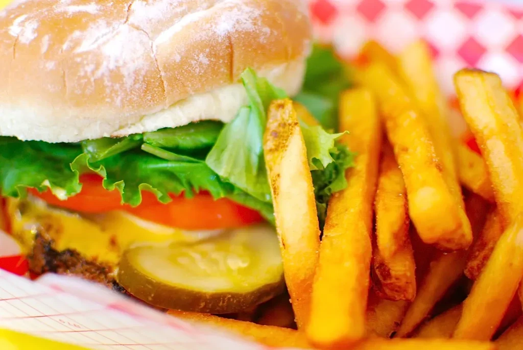 Cheeseburger with pickles, lettuce, tomato, and French fries in a red basket.