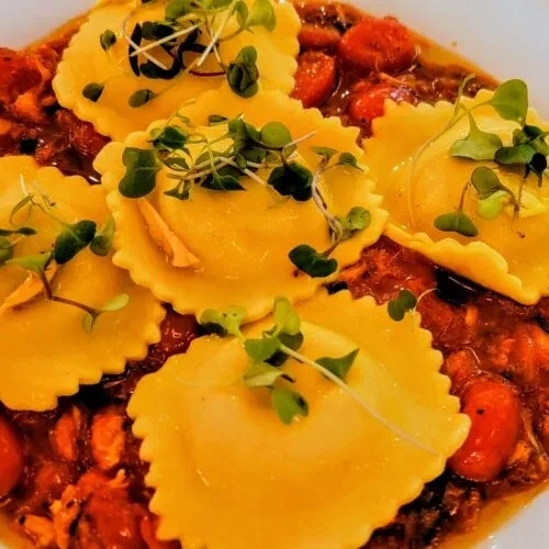 Overhead six yellow-orange ravioli with herbs in a reddish-brown sauce.