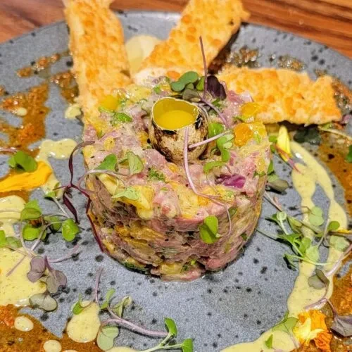 Molded tartare with quail egg, microgreens, sauces, and crostini.