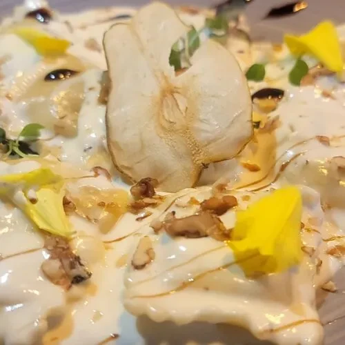 Pasta dish with creamy sauce, dried pear, walnuts, herbs, and edible flowers.