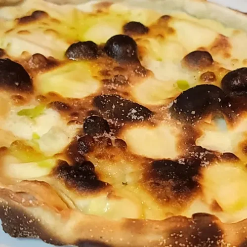 Close-up: Golden pizza with melted cheese, dark spots, salt, and green herbs.