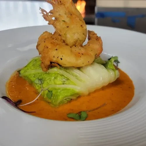 Golden-brown fried shrimp on lettuce in creamy orange sauce with microgreens.