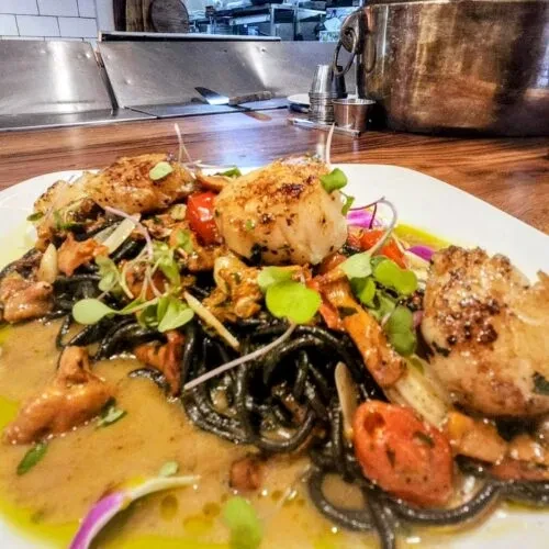 Black spaghetti topped with seared scallops, microgreens, and tomatoes.