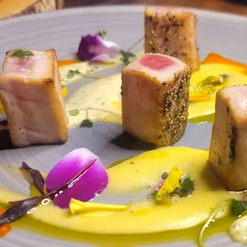 Meticulously plated pepper-crusted rare tuna with sauces, flowers, and herbs.