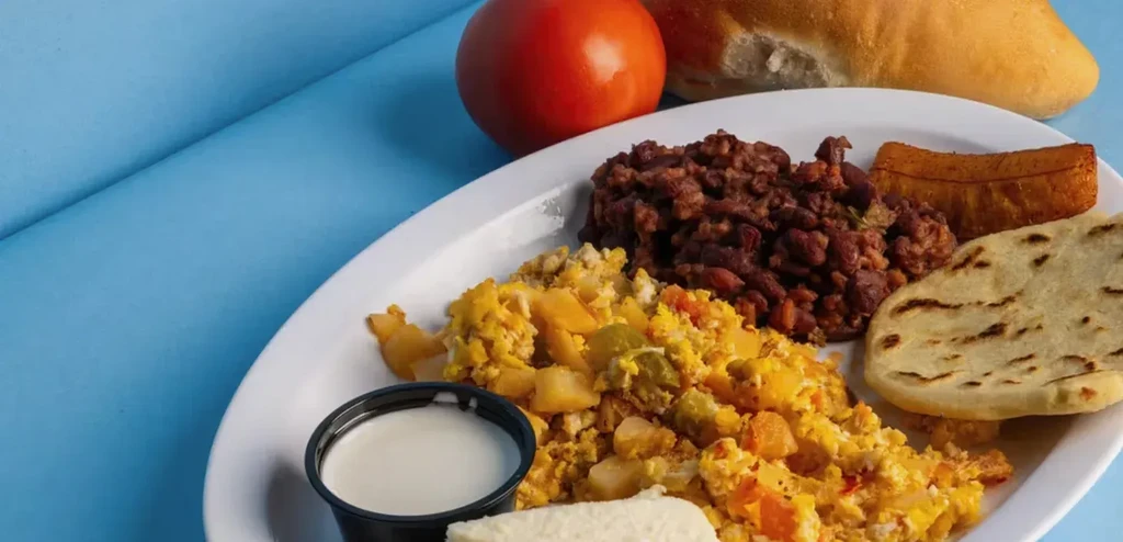 Breakfast plate with scrambled eggs, beans, plantain, flatbread, cheese, crema.