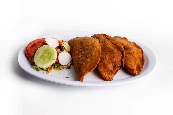Plate with three golden empanadas and fresh vegetable salad.