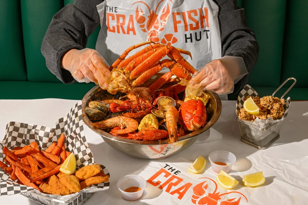 Person wearing a bib eats seafood boil with crab, crawfish, corn.