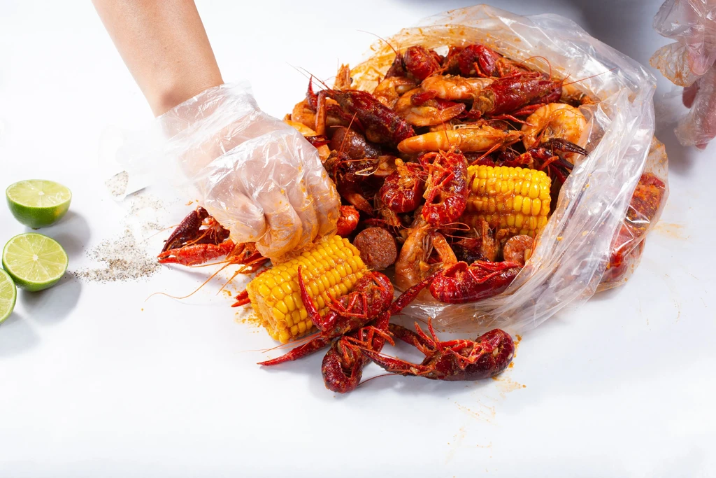 Gloved hands serve seasoned crawfish, shrimp, corn seafood boil.